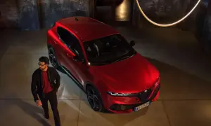 Elegancki mężczyzna w okularach obok lśniącego, czerwonego Alfa Romeo Tonale. Stylowy duet w industrialnym wnętrzu.