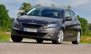 Ciemnoszary Peugeot 308 2015 z polskimi tablicami WE 859KV jedzie po drodze wśród zieleni.