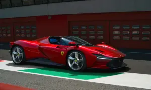 Czerwone Ferrari SP3 na torze wyścigowym, z niebieskimi siedzeniami i garażami w tle.