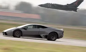 Szary Lamborghini Reventon pędzi po pasie startowym, gdy myśliwiec Tornado przelatuje nad nim.