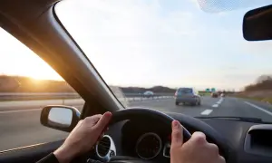 Ręce na kierownicy Toyoty Corolli, słońce zachodzi na autostradzie. Jak włączyć tempomat?