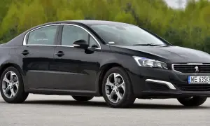 Elegancki, czarny Peugeot 508 z chromowanymi detalami i felgami stoi na tle zieleni.