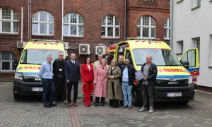Grupa osób pozuje przed dwoma ambulansami. Jeden z mężczyzn trzyma dokument, być może związany z czn rejestracja.