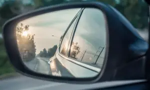 Widok z lusterka bocznego Toyoty. Słońce odbija się w szybie, a droga wije się w oddali.