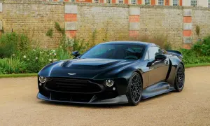 Elegancki, czarny Aston Martin Victor prezentuje się majestatycznie na tle zabytkowego dworu i bujnej zieleni.