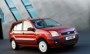 Czerwony Ford Fusion 1.4 benzyna w ruchu, z kobietą za kierownicą, na tle nowoczesnego budynku.