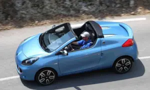 Niebieski kabriolet Renault Wind z otwartym dachem, kierowca w czapce i niebieskiej koszulce jedzie po krętej drodze.