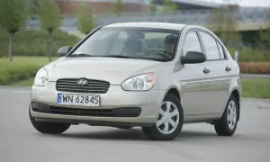 Złoty Hyundai Accent z kierowcą za kierownicą, zaparkowany na zewnątrz.