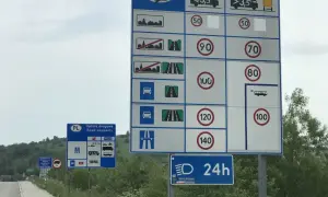 Znaki drogowe informujące o opłatach i limitach prędkości na drodze dwujezdniowej.