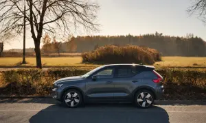 Szary Volvo EX40 zaparkowany na poboczu drogi, w tle jesienny krajobraz z drzewami i krzewami.