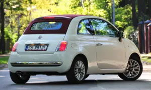Biały fiat 500c z bordowym dachem stoi na drodze, otoczony zielenią drzew.