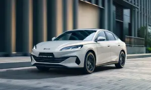 Biały BYD Seal 6 DM-i sunie ulicą, otoczony miejską architekturą i zielenią.