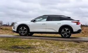 Biały Citroen C5X na tle pochmurnego nieba i wiejskiego krajobrazu. Elegancki design i nowoczesne felgi podkreślają jego wyjątkowość.