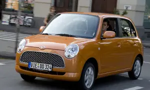 Pomarańczowy Daihatsu Trevis z kierowcą za kierownicą jedzie ulicą.