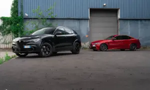 Dwa sportowe Alfa Romeo: czarny Stelvio Quadrifoglio i czerwona Giulia, stoją przed budynkiem z niebieską, falistą fasadą.