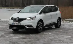 Biały Renault Initiale na oblodzonym podjeździe, z widokiem na zamarznięte jezioro i drzewa.