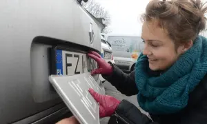 Kobieta w czerwonych rękawiczkach montuje tablicę rejestracyjną. KSU rejestracja w toku.