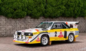 Biało-żółty Audi Sport Quattro z numerem 2, gotowy do rajdu, z licznymi światłami i logotypami sponsorów.