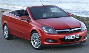 Czerwony opel cabrio z opuszczonym dachem, zaparkowany przy plaży. Kobieta za kierownicą cieszy się jazdą.