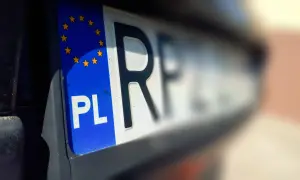 Zbliżenie na polską tablicę rejestracyjną z symbolem UE. Litery "PL" i fragment kolejnych liter są wyraźne, reszta tablicy rozmyta.