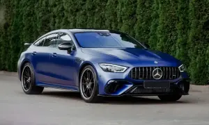Matowy, granatowy Mercedes E63 AMG z czarnymi felgami stoi na tle zielonego żywopłotu.