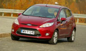 Czerwony Ford Fiesta 2010 z kierowcą za kierownicą, jadący po drodze.