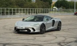 Srebrny McLaren GT z czarnym dachem, zaparkowany na placu z widocznymi śladami opon.