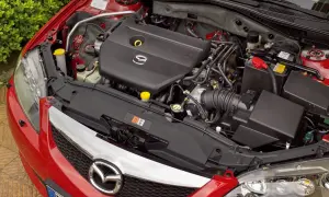 Silnik Mazdy 6 GG, czarny plastikowy kolektor dolotowy z logo Mazda, akumulator i elementy układu chłodzenia.