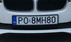 Białe auto z tablicą rejestracyjną PO 8MH80. W tle kratka grilla.