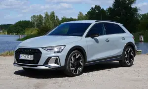 Jasnoszary Audi A3 allstreet stoi na żwirowej drodze nad jeziorem.