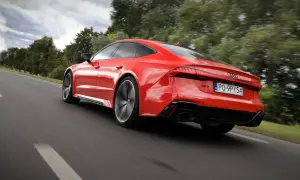 Czerwone Audi RS 7 pędzi po drodze, otoczone zielenią drzew.