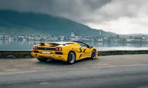 Żółty Lamborghini Diablo SV z czarnymi akcentami stoi nad jeziorem, w tle miasteczko i góry.