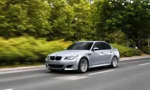 Srebrne BMW M5 V10 pędzi po drodze, otoczone zielenią drzew i krzewów.