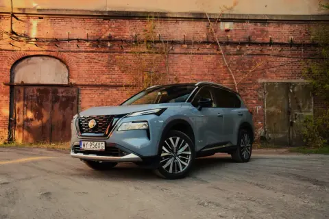 Szary Nissan X-Trail stoi przed starą ceglaną ścianą z zardzewiałymi drzwiami.