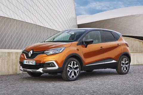 Pomarańczowy Renault Captur 2016 z czarnym dachem zaparkowany na brukowanej nawierzchni przed nowoczesnym budynkiem.