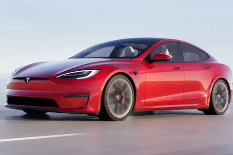 Czerwony Tesla Plaid pędzi po drodze, z widokiem na morze i góry w tle.