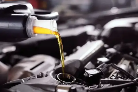 Wlewam olej do silnika Toyoty Yaris 1.0. Złoty płyn spływa z butelki do otworu.