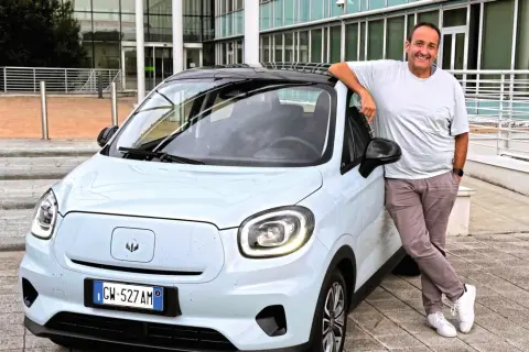 Uśmiechnięty mężczyzna opiera się o jasny samochód elektryczny Leapmotor T03.