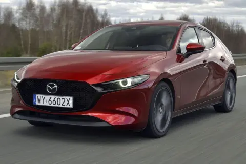 Czerwona Mazda 3 2.0 150KM w ruchu. Kierowca za kierownicą, dynamiczna jazda po drodze.
