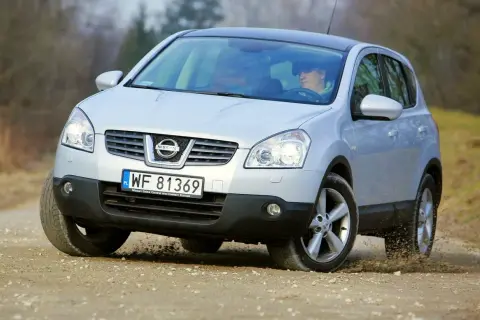 Srebrny Nissan Qashqai 2.0 benzyna pokonuje zakręt na piaszczystej drodze, wzbijając kurz.