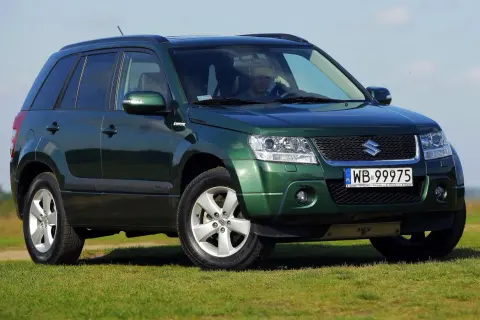 Zielony Suzuki Grand Vitara 2 na tle błękitnego nieba i zielonej trawy.