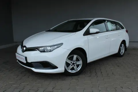 Biała Toyota Auris II 1.6 132 KM, kombi, na chodniku. Wiele osób szuka o niej pozytywnych opinii.