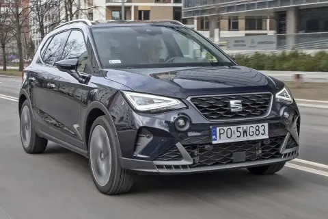 Ciemnoniebieski Seat Arona w ruchu miejskim. Kierowca w okularach. Wiele pozytywnych seat arona opinie potwierdza jego miejski charakter.