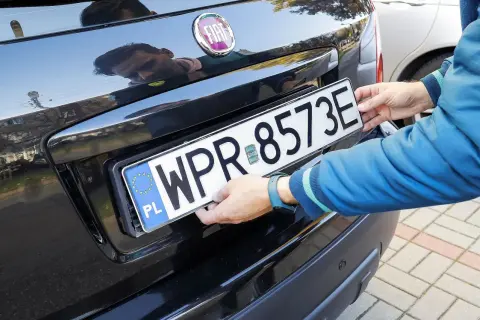 Ręce montują tablicę rejestracyjną WPR 8573E do czarnego Fiata. Zgubiona tablica rejestracyjna została odnaleziona.