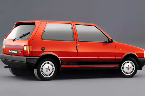 Pomarańczowy Fiat Uno Turbo Le. z czarnymi pasami na boku i felgami w stylu retro.