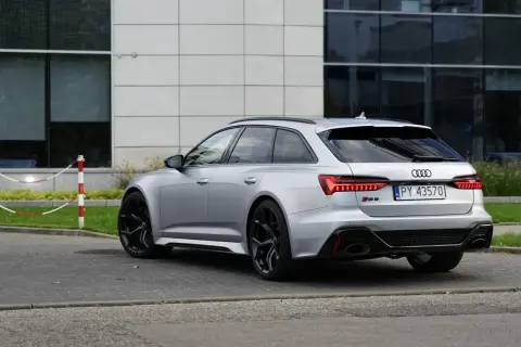Srebrne Audi RS6 Avant z czarnymi felgami stoi na parkingu przed nowoczesnym budynkiem.