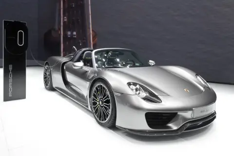Srebrny Porsche 918 Spyder z zielonymi akcentami na felgach, gotowy do ładowania przy stacji Porsche.