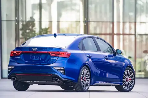 Niebieskie Kia Forte GT z czerwonymi akcentami, zaparkowane przed nowoczesnym budynkiem.