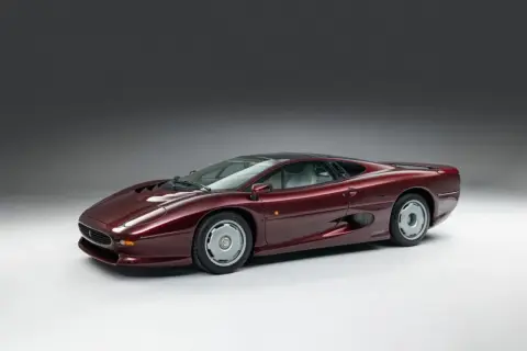 Bordowy Jaguar XJ220, ikona lat 90., prezentuje swoje aerodynamiczne linie na tle szarego studia.