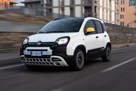 Biały Fiat Panda 3 z żółtym lusterkiem jedzie po drodze.